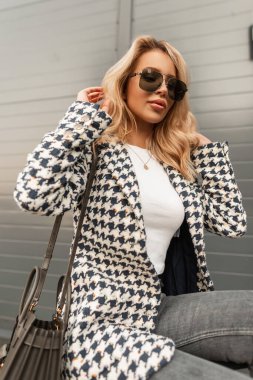 Beautiful girl model hipster with sunglasses in a fashionable coat with a white T-shirt and a bag in the city