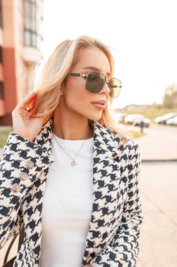 Güneşli bir yaz portresi. Güneş gözlüklü, şık bir kadın. Gün batımında sokakta yürüyor.