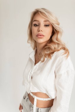 Stüdyoda beyaz bir arka planda şık bir beyaz gömlekle güzel görünümlü ve makyajlı kendine güvenen güzel bir kızın kadın portresi.