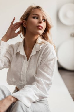 Beautiful sexy model woman with makeup in fashionable stylish clothes with a shirt and jeans sitting in the studio
