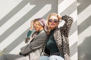 Şık sonbahar kıyafetleri içinde klasik güneş gözlüklü güzel, genç moda kadın kız arkadaşlar güneşli bir günde sokakta eğleniyorlar.