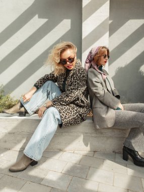 Tarz, Moda ve Güzellik. Güneşli bir bahar gününde iki güzel hippi şık gündelik kıyafetler içinde paltolar, kotlar ve ayakkabılar içinde şehirde otururlar.