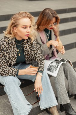 Güzel, şık giyinmiş genç kızlar basamaklarda oturuyor, kahve içiyor ve şehirde dergi okuyor.