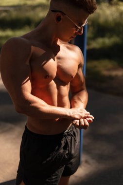 Seksi kaslı vücutlu yakışıklı sporcu. Güneş gözlüklü, şortlu, açık havada poz veren.