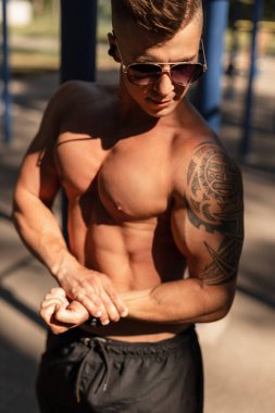 Saç stili ve moda güneş gözlüklü, kolunda çıplak kaslı gövde ve Maya dövmesi olan şık vücutlu hippi. Poz veriyor ve dışarıda çalışıyor.