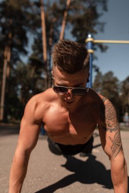 Atletik kaslı genç adam parkta antrenman yapıyor ve şınav çekiyor.