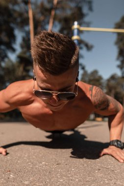 Atletik kaslı genç adam parkta antrenman yapıyor ve şınav çekiyor.