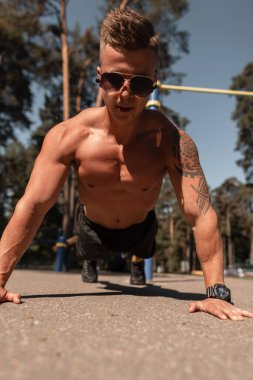 Atletik kaslı genç adam parkta antrenman yapıyor ve şınav çekiyor.