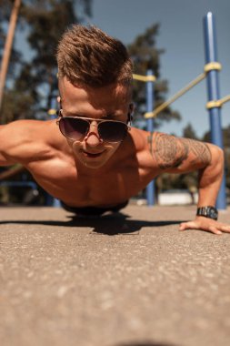 Atletik kaslı genç adam parkta antrenman yapıyor ve şınav çekiyor.