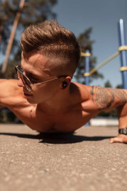 Kaslı vücutlu, güneş gözlüklü, kulaklıklı, müzik dinleyen ve dışarıda şınav çeken yakışıklı genç bir sporcu. Spor adamı egzersizi.