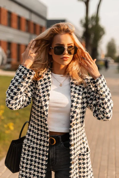美丽的年轻迷人的金发姑娘 戴着时髦的太阳镜 头戴手提包 日落时分在城里散步 — 图库照片