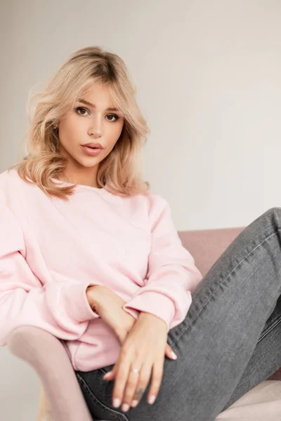 俊俏可爱的女模特 脸蛋漂亮 穿着时髦的粉色毛衣 牛仔裤风格 坐在室内的粉红复古扶手椅上 — 图库照片