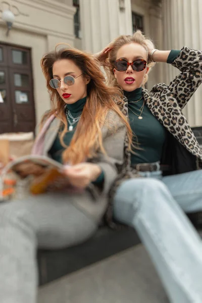Duas lindas garotas da moda em óculos e roupas modernas posando com óculos  para a imagem da câmera de meninas elegantes em óculos