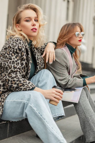 Şık giyinmiş, güneş gözlüklü iki güzel genç kız şehrin basamaklarında oturur, kahve içer ve dergi okurlar.