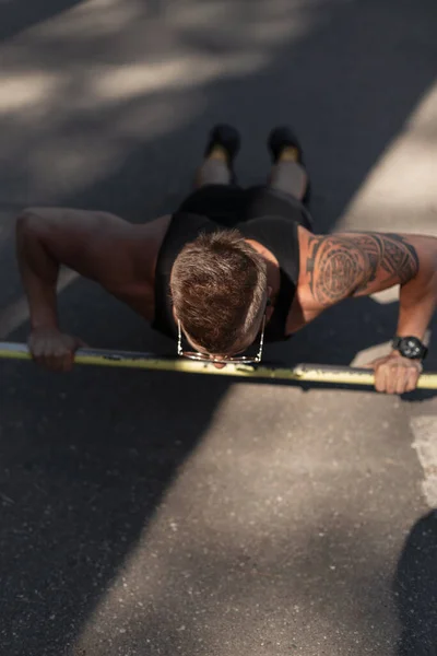 Handsome young muscular man workout doing push-ups and exercising on asphalt in the street at sunlight