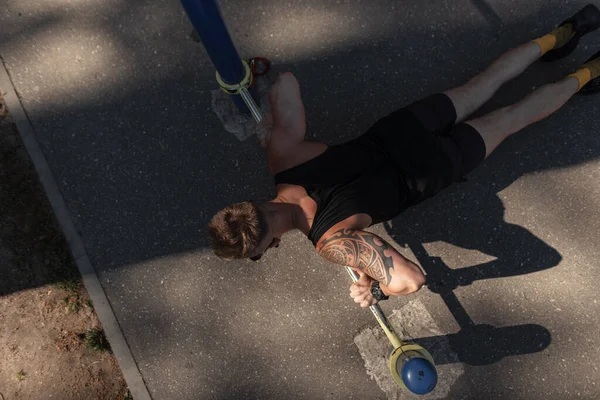 Sporty young man with a tattoo in black clothes does push-ups on the pavement, top view. Healthy lifestyle concept