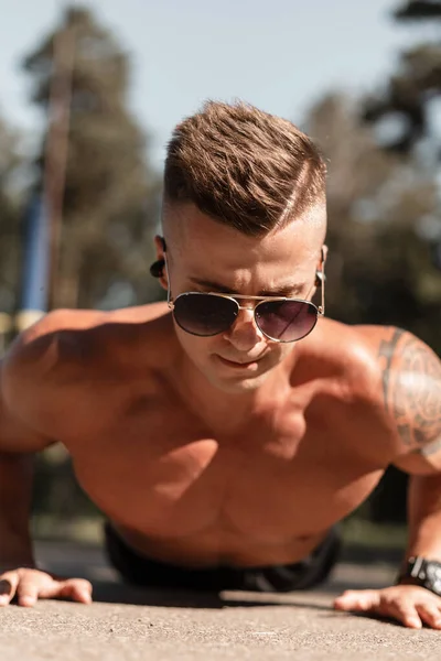 Handsome young athlete man with hairstyle and fashionable sunglasses doing push-ups on the street