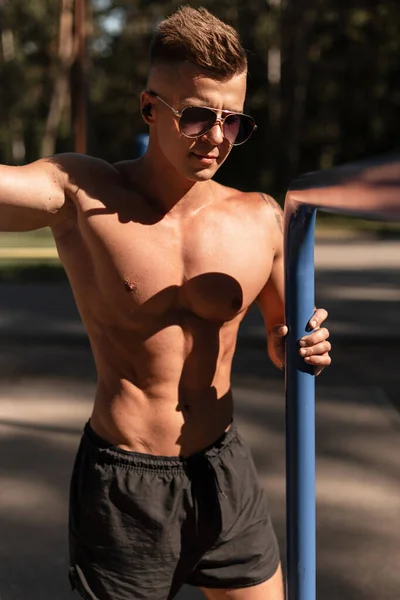 ハンサムなフィットネス男モデルでファッションサングラスともにセクシー筋肉体屋外で日没 — ストック写真