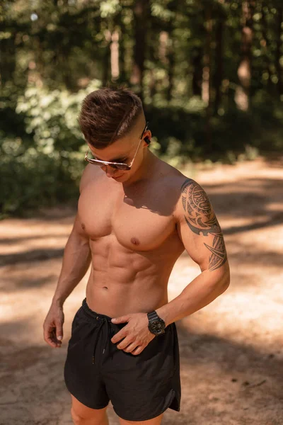 잘생긴 보디빌더 선수가 선글라스를 근육질의 헤드폰을 문신은 밖에서 운동을 듣는다 — 스톡 사진