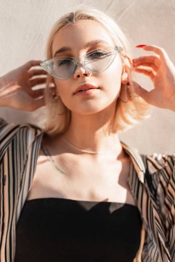 Moda tişörtlü, siyah bluzlu ve duvarın yanında poz veren havalı genç bir kadının şık portresi.