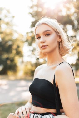 Parlak moda portresi. Kısa saçlı, siyah kolsuz tişörtlü güzel bir kadın. Güneşli bir günde parkta yürüyor.