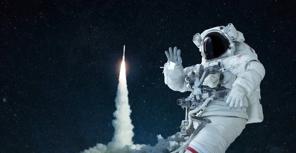 Space man in a space suit and hat travels in open space and waves his hand against the background of a rocket lift off. Spaceship takes off successfully. Welcome to space, concept