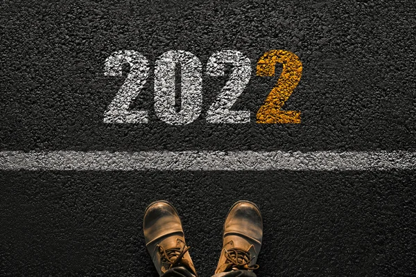 New year 2022, concept. Man takes the first step in the new year. Men\'s shoes on the asphalt near the line with the numbers 2022, creative idea.