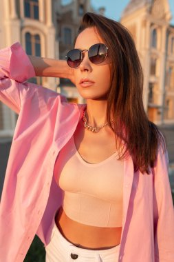 Moda gözlüklü, modaya uygun pembe gömlekli ve günbatımında şehirde yürüyüş yapan seksi moda genç kadın modeli. Kentsel kadın tarzı
