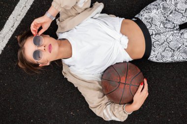 Havalı spor kıyafetleri, rüzgarlığı, tişörtü, tozluğu ve kaldırımda duran ve gözlük takan güzel, genç ve seksi hippi kadın.