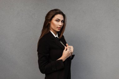 Modaya uygun siyah takım elbiseli, sokakta gri arka planda ceketi olan güzel bir kız.