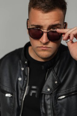 Süslü siyah elbiseli yakışıklı bir adamın güneş gözlüğüyle kameraya bakarken güzel bir portresi.