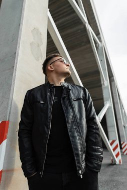 Güneş gözlüklü, deri ceketli ve kot pantolonlu şık, yakışıklı bir adam sokakta yürüyor. Şehir erkeği kıyafetlere bakar.