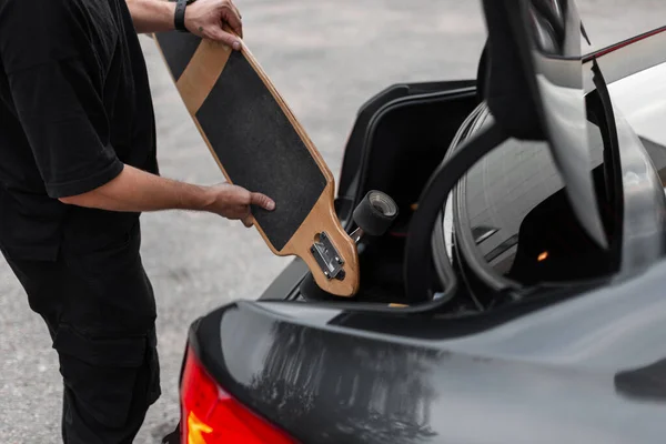 Hipster Man Black Clothes Puts Longboard Trunk Car Active Weekends — Stock Photo, Image