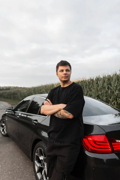 Handsome man stands near a car outdoors. Guy travels by the car