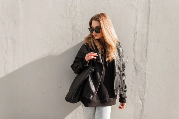 流行の革のジャケット パーカーと黒のバッグで美しい女性ヒップスターのファッション都市の肖像画は 通りの灰色の壁の近くに立つ 女性の春服 ファッションと美しさ — ストック写真