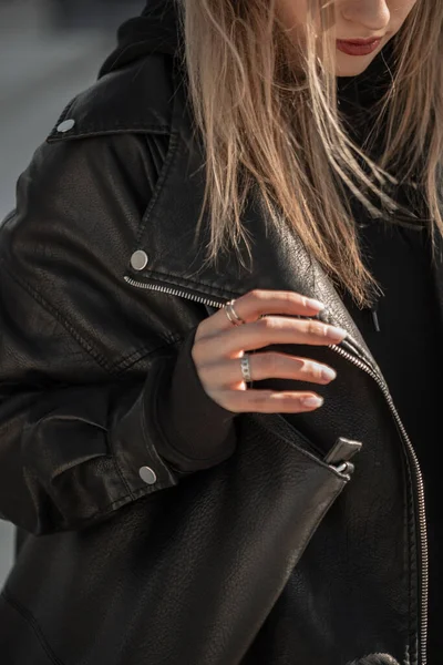 Female hipster model in a fashionable black leather jacket with a leather bag walks in the city.   woman\'s hand with a silver ring jewelry and manicure. Trendy girl