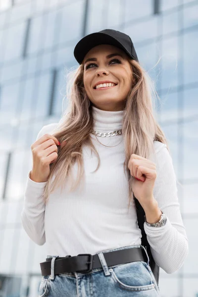 Happiness urban woman with white smile in casual clothes with cap, jeans and white sweater walks and travels in the city