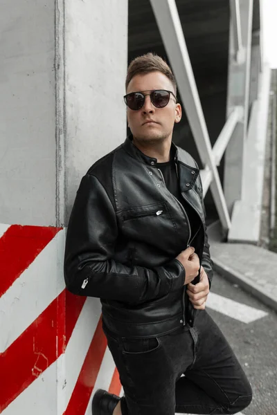 时尚都市男子 身穿黑色衣服 皮夹克 戴着时髦太阳镜 站在混凝土大楼附近的街上 — 图库照片
