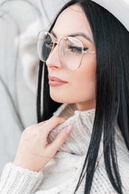 Şık bir süveter giymiş, şapkası ve gözlüğü olan güzel bir kız sokakta yürüyor.