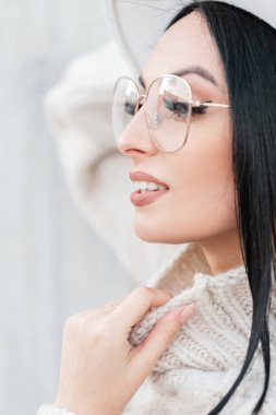 Uzun saçlı, hoş, beyaz, klasik süveterli, gri arka planda moda gözlüklü güzel bir kızın mutlu portresi.