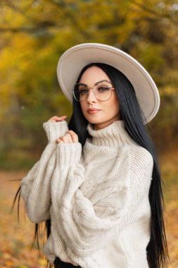 Şık bir bej şapka ve örgü süveter giyen ve bir sonbahar parkında poz veren şık bir kadın modelinin muhteşem sonbahar kadın portresi. Moda kadın kıyafetleri.