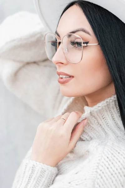 美しい顔とヴィンテージのメガネを持つ若い白人の少女の肖像画でファッショナブルなニットの服帽子と白いセーターグレーの背景 — ストック写真