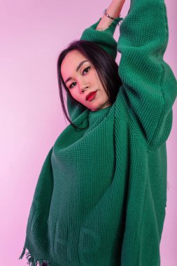 Pembe arka planda yeşil stil örülmüş süveter giyen güzel Asyalı kız model.
