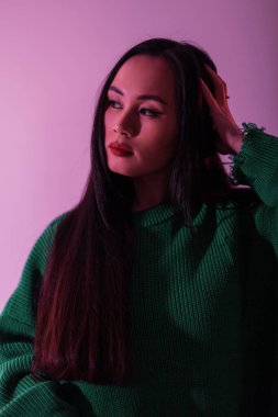 Süslü, yeşil örgü süveter giyen Asyalı model kız stüdyoda pembe ışıkla. Renkli kadın portresi