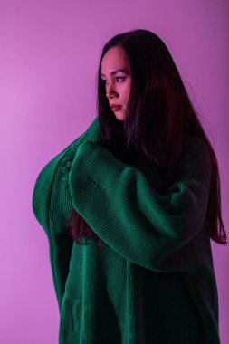 Stüdyoda pembe ışıklarla örülmüş yeşil süveterli güzel bir Asyalı kız modeli.