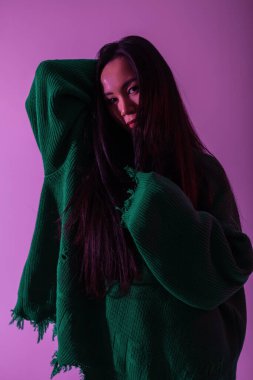 Moda modası geçmiş, yırtık pırtık yeşil kazaklı, pembe ışıklı Asyalı bir kadın. Renkli kadın portresi