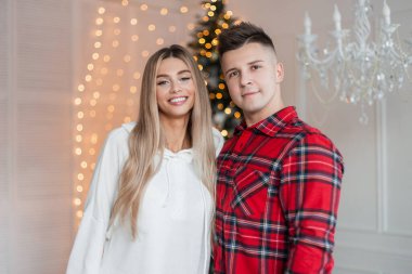 Mutlu, güzel, güler yüzlü bir kız. Moda elbiseli yakışıklı bir adamla evde, Noel ışıklarının yanında.