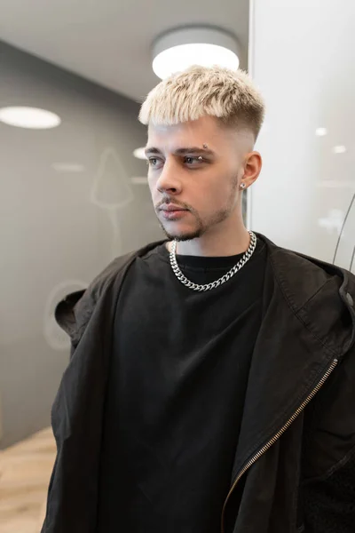 Handsome young man with hair in black trendy clothes with black t-shirt and black hoodie indoors