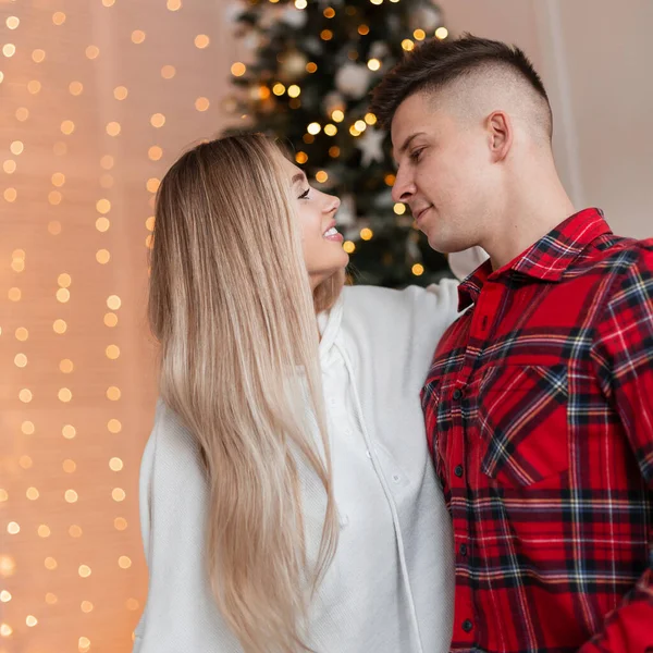 Beautiful young couple in fashion outfit hugging and ready to kiss on a background of Christmas decorations