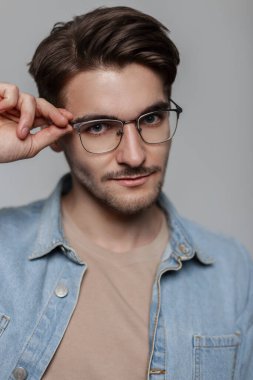 Tarafsız gri bir arkaplanda eski moda güneş gözlüğü takan, modaya uygun bir kot giyen yakışıklı, modaya uygun bir hippinin portresi.